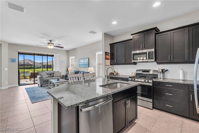 kitchen with a kitchen island with sink, sink, decorative backsplash, appliances with stainless steel finishes, and ceiling fan