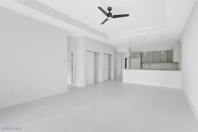 unfurnished living room featuring ceiling fan, a raised ceiling, and sink