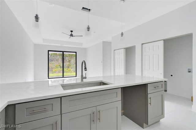 kitchen with gray cabinetry, a tray ceiling, sink, and ceiling fan