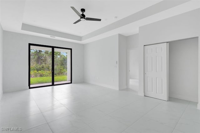 unfurnished bedroom featuring a closet, a tray ceiling, ceiling fan, and access to outside