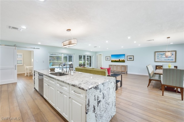 kitchen with pendant lighting, sink, white cabinetry, a barn door, and light hardwood / wood-style flooring