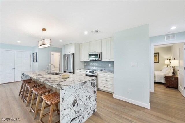 kitchen with light wood-type flooring, a kitchen island with sink, sink, white cabinetry, and appliances with stainless steel finishes