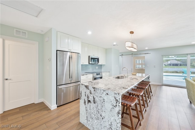 kitchen with sink, white cabinetry, stainless steel appliances, a barn door, and light hardwood / wood-style floors