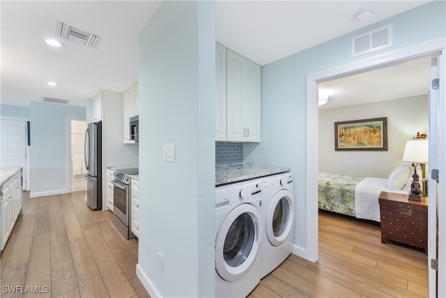 laundry room featuring light wood-type flooring, independent washer and dryer, and cabinets