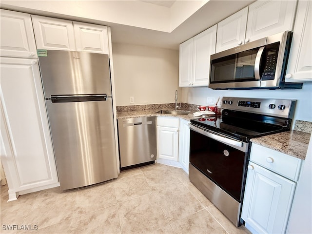 kitchen with light stone countertops, stainless steel appliances, white cabinets, sink, and light tile patterned floors