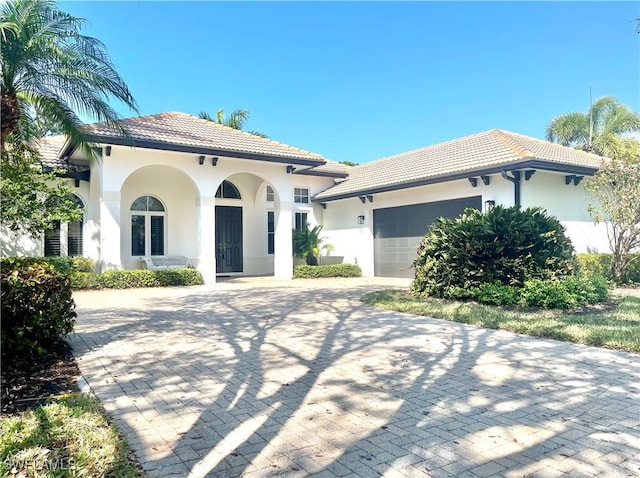 mediterranean / spanish-style house with stucco siding, a tiled roof, an attached garage, and decorative driveway