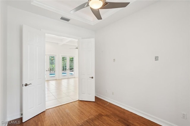 empty room featuring baseboards, ceiling fan, wood finished floors, a raised ceiling, and french doors