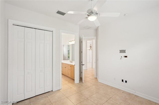 unfurnished bedroom with light tile patterned floors, a closet, a sink, baseboards, and ceiling fan