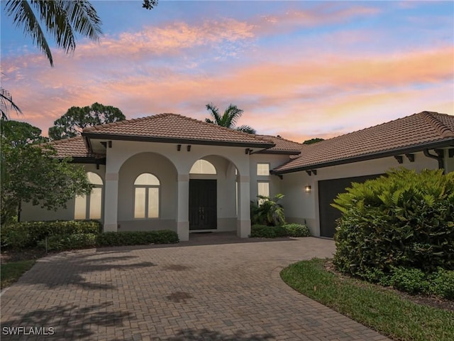 mediterranean / spanish-style house featuring a tile roof, decorative driveway, stucco siding, and a garage