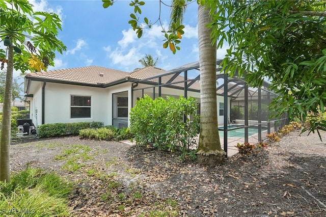 back of property featuring a tiled roof, stucco siding, an outdoor pool, and glass enclosure