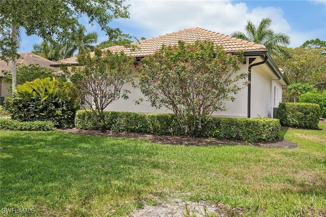 view of side of property with a lawn, a tiled roof, and stucco siding