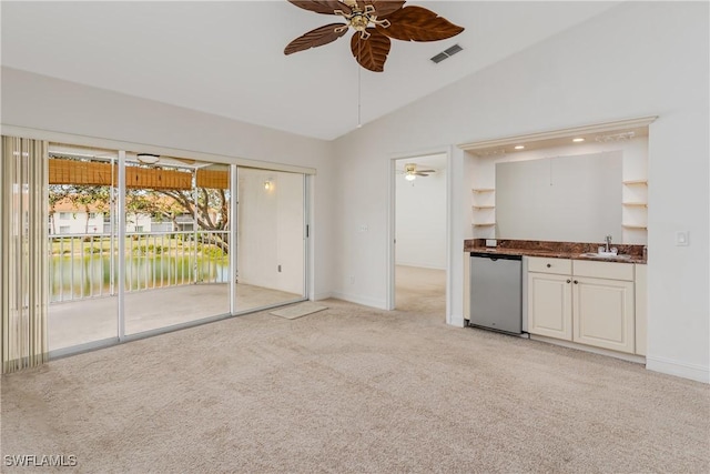 unfurnished living room with sink, a water view, lofted ceiling, ceiling fan, and light colored carpet