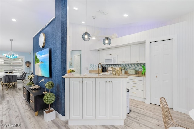 kitchen with light wood-type flooring, white cabinets, and decorative light fixtures