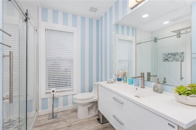 bathroom with hardwood / wood-style floors, a shower with door, vanity, and toilet