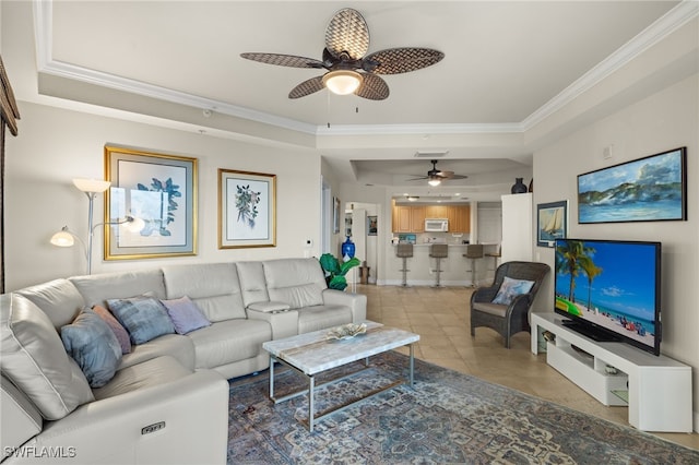 living room with ceiling fan, a raised ceiling, ornamental molding, and light tile patterned floors