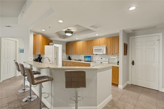 kitchen featuring white appliances, sink, a raised ceiling, kitchen peninsula, and a breakfast bar area