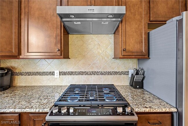 7638 Jacaranda Ln, Naples, FL 34114 - kitchen featuring light stone counters, tasteful backsplash, appliances with stainless steel finishes, brown cabinets, and exhaust hood
