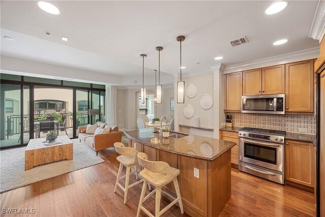 kitchen with sink, stone countertops, decorative light fixtures, appliances with stainless steel finishes, and a kitchen island with sink