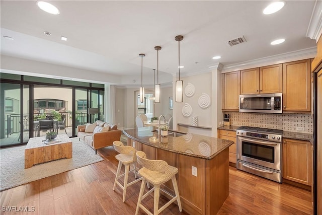 kitchen featuring sink, stone countertops, decorative light fixtures, appliances with stainless steel finishes, and a kitchen island with sink