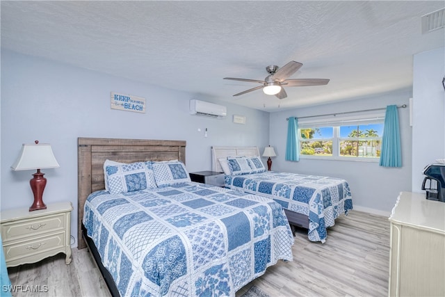 bedroom with ceiling fan, a textured ceiling, light hardwood / wood-style floors, and a wall mounted AC