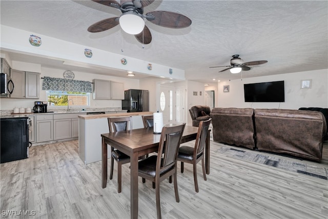 dining space featuring light hardwood / wood-style flooring, ceiling fan, sink, and a textured ceiling