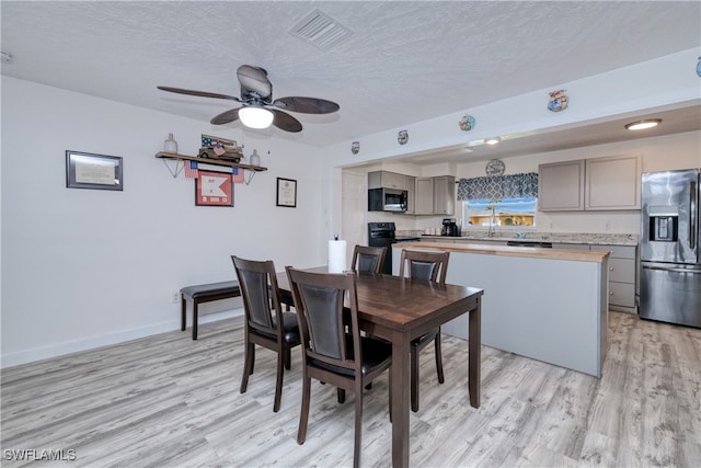 dining space with light wood-type flooring, ceiling fan, sink, and a textured ceiling