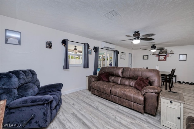 living room featuring a textured ceiling, an AC wall unit, ceiling fan, and light hardwood / wood-style flooring