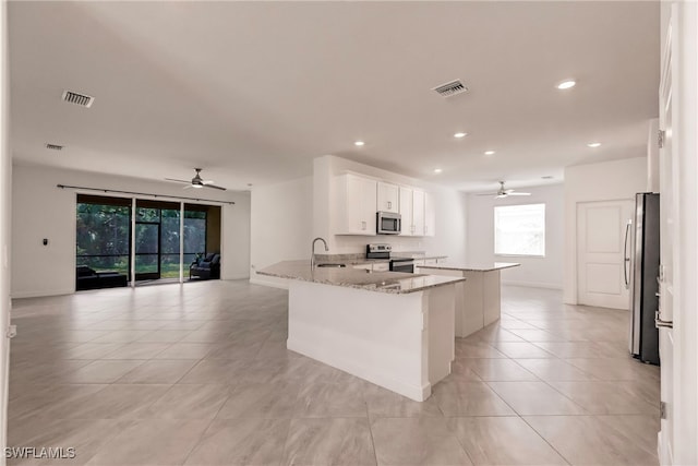 kitchen with kitchen peninsula, sink, white cabinetry, appliances with stainless steel finishes, and light stone counters