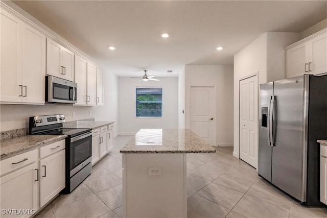 kitchen with a kitchen island, stainless steel appliances, white cabinetry, light stone counters, and ceiling fan