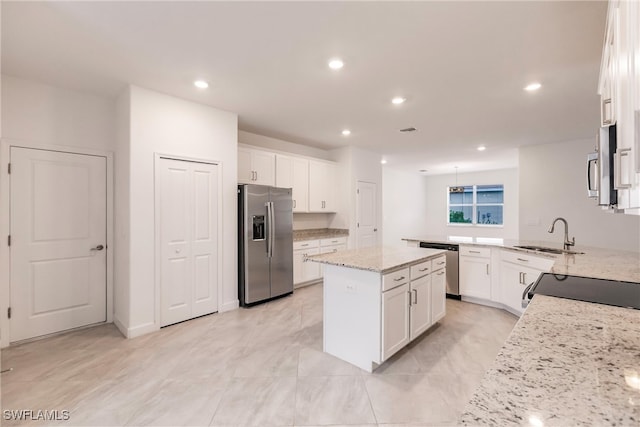 kitchen featuring appliances with stainless steel finishes, white cabinets, light stone counters, and a kitchen island