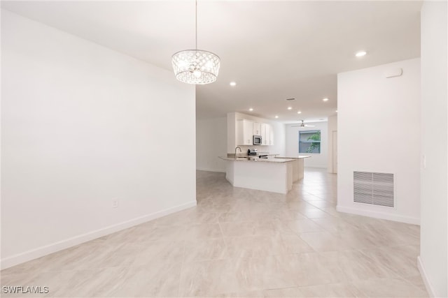 interior space with a notable chandelier, decorative light fixtures, kitchen peninsula, and white cabinets