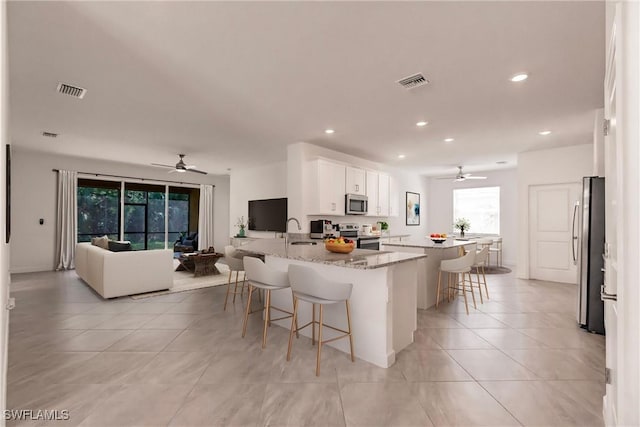 kitchen with visible vents, white cabinets, light stone counters, a breakfast bar, and stainless steel appliances