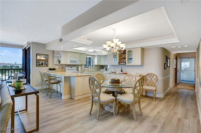 dining space featuring a notable chandelier, light wood-type flooring, and a tray ceiling