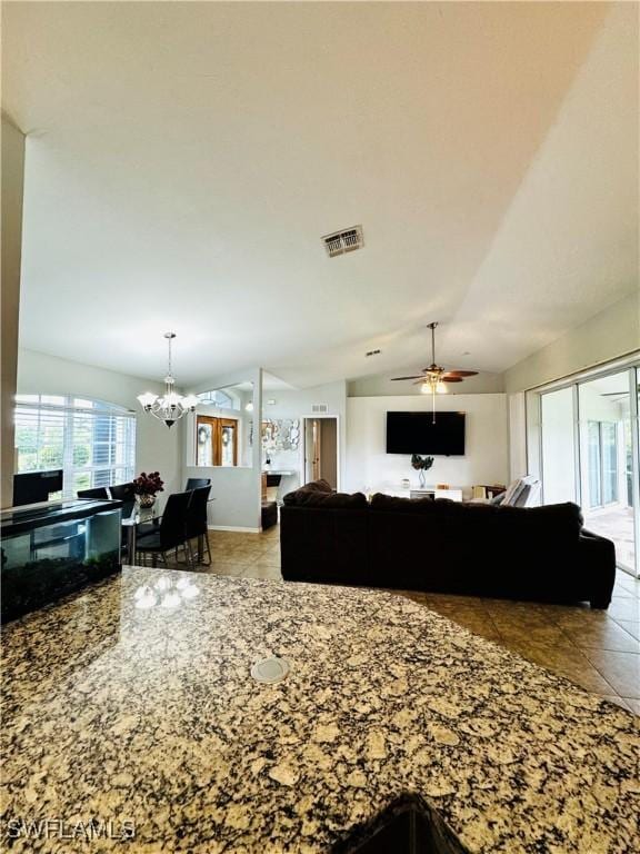 tiled living room featuring ceiling fan with notable chandelier and vaulted ceiling