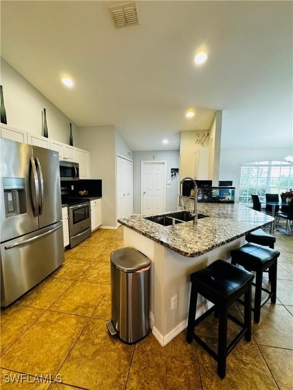 kitchen with white cabinets, sink, a breakfast bar area, light stone countertops, and stainless steel appliances