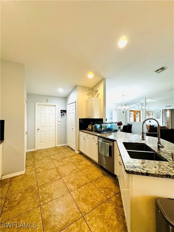 kitchen featuring stainless steel dishwasher, sink, stone countertops, decorative light fixtures, and white cabinetry