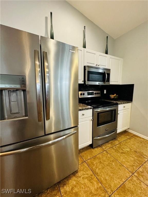 kitchen with white cabinets, appliances with stainless steel finishes, light tile patterned flooring, and dark stone countertops