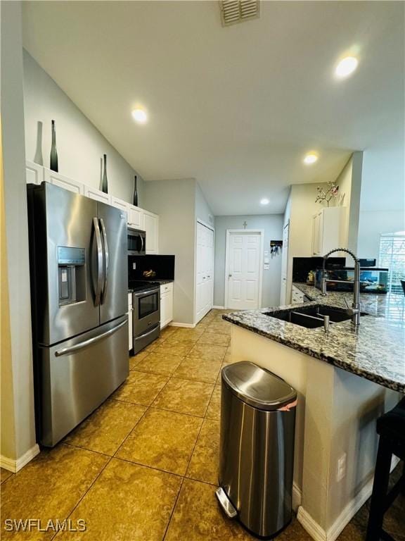 kitchen with a breakfast bar, white cabinets, sink, dark stone countertops, and stainless steel appliances