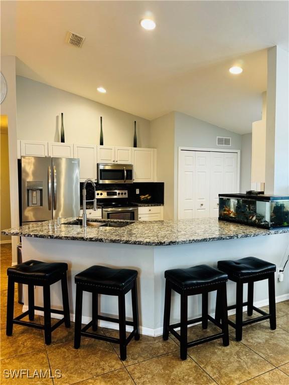 kitchen featuring dark stone counters, vaulted ceiling, white cabinetry, kitchen peninsula, and stainless steel appliances