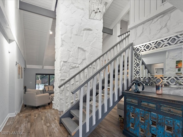 stairway with wood-type flooring, beamed ceiling, and a notable chandelier