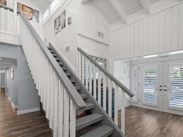 staircase with wood walls, beam ceiling, french doors, high vaulted ceiling, and hardwood / wood-style floors