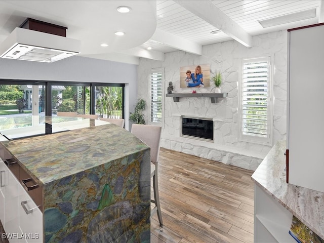 kitchen with light stone counters, beam ceiling, french doors, a fireplace, and hardwood / wood-style floors