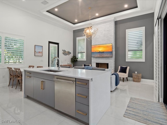 kitchen with a stone fireplace, an island with sink, sink, and gray cabinets