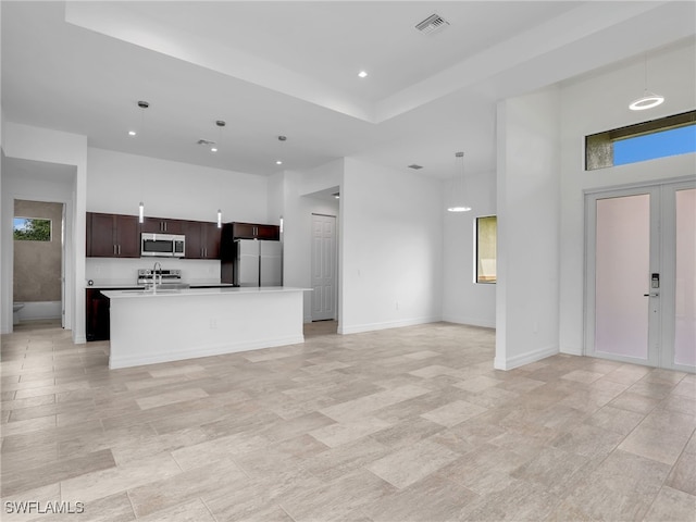 kitchen with white refrigerator, hanging light fixtures, dark brown cabinets, a kitchen island with sink, and a high ceiling