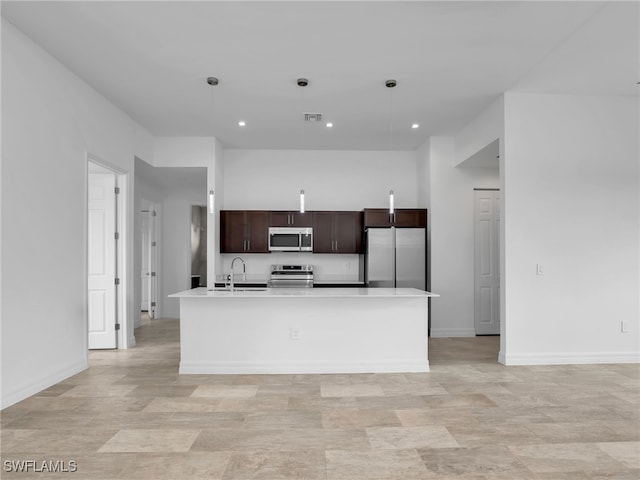 kitchen featuring appliances with stainless steel finishes, an island with sink, pendant lighting, dark brown cabinets, and sink