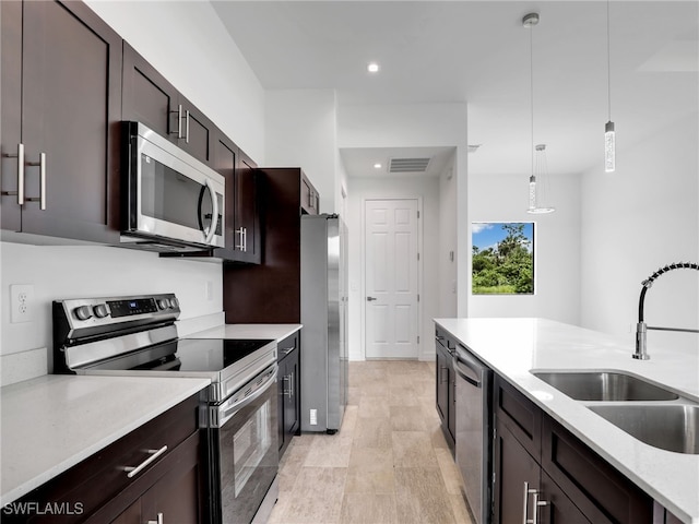 kitchen featuring dark brown cabinetry, hanging light fixtures, sink, light hardwood / wood-style flooring, and stainless steel appliances