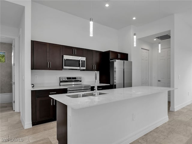 kitchen with light stone countertops, a center island with sink, appliances with stainless steel finishes, and hanging light fixtures