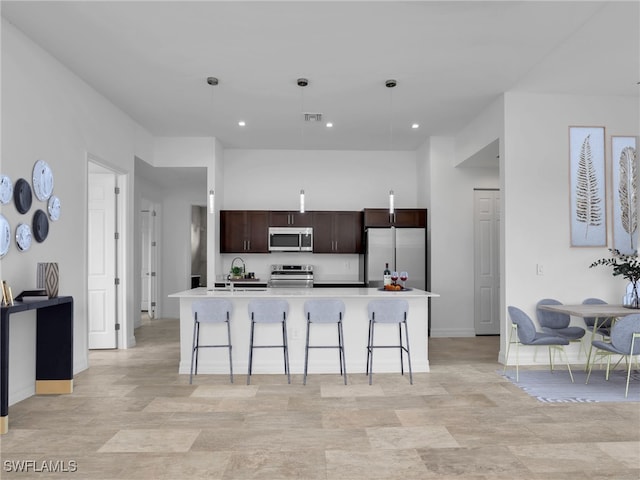 kitchen with hanging light fixtures, a center island with sink, a kitchen bar, and stainless steel appliances