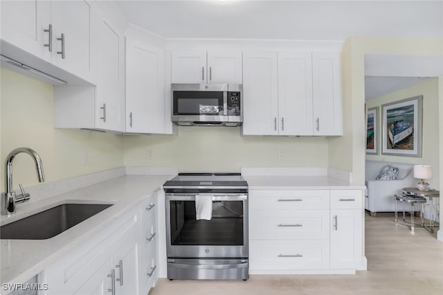 kitchen with light stone counters, sink, white cabinetry, light hardwood / wood-style flooring, and appliances with stainless steel finishes