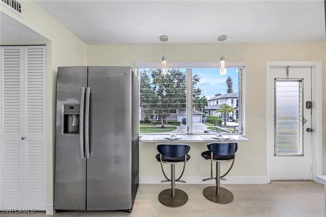 kitchen with light hardwood / wood-style floors, stainless steel refrigerator with ice dispenser, a breakfast bar, and decorative light fixtures